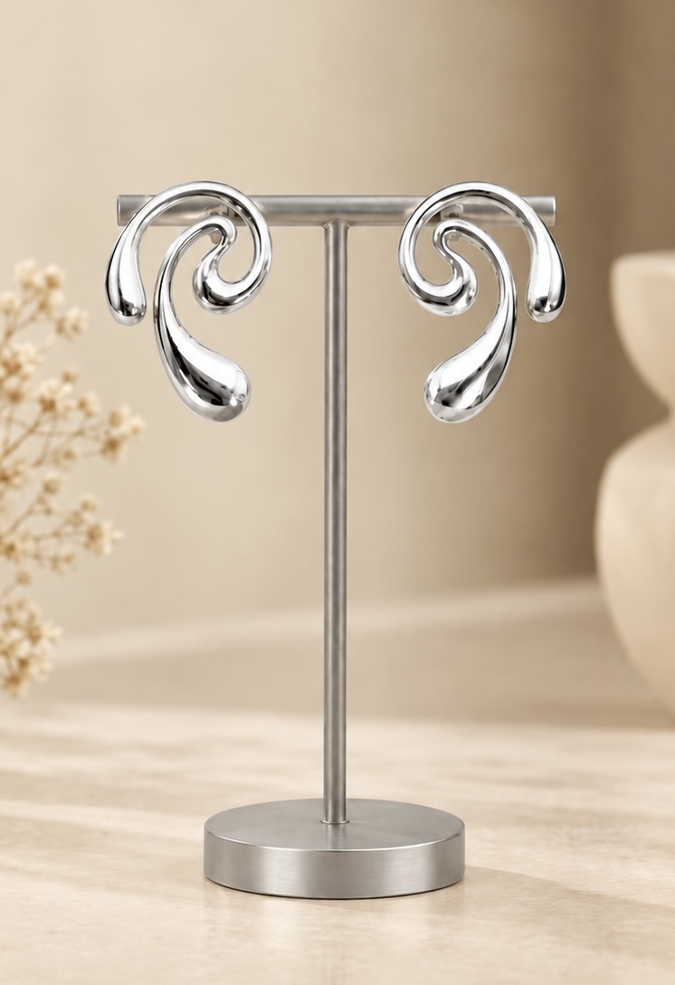 Spiral silver-tone swirl drop earrings with a mirror finish on a stand against a warm ivory backdrop