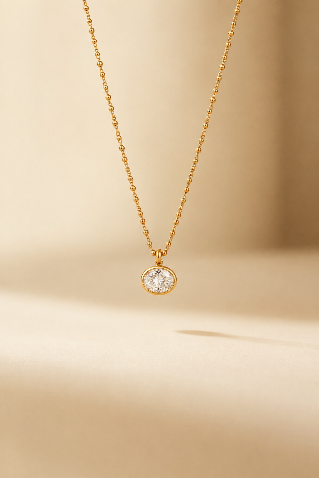Lucienne gold-tone necklace with a round clear crystal pendant on a warm ivory studio backdrop