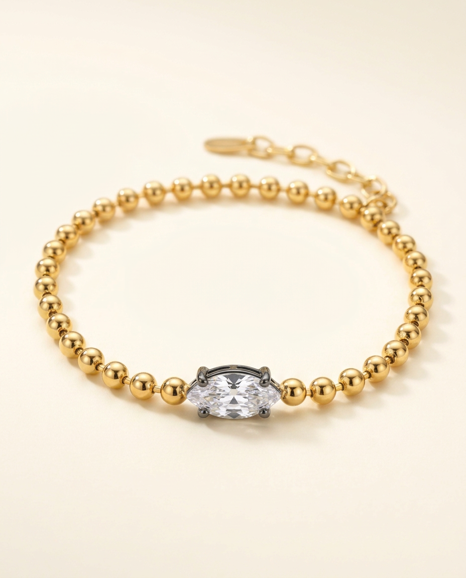 Celeste gold-tone ball-chain bracelet with one clear marquise-cut stone on a warm ivory studio backdrop